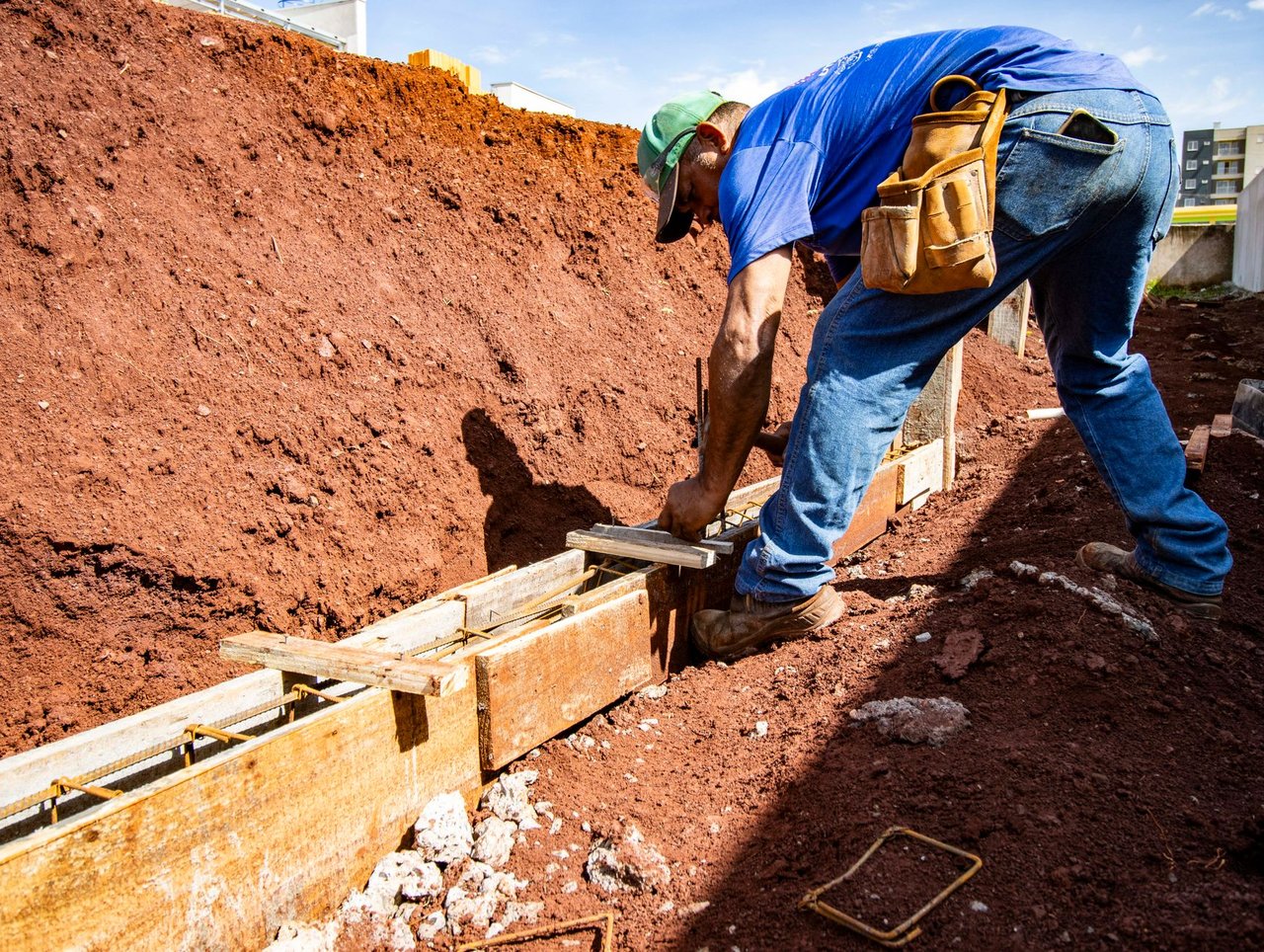 Trabalhador da construção civil atua na preparação da fundação de uma obra ao ar livre.