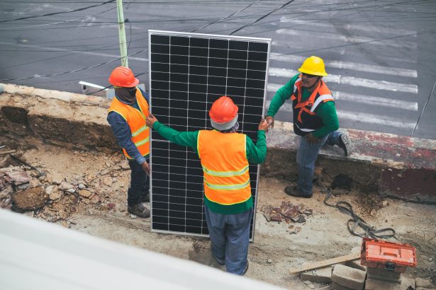 Trabalhadores usando equipamentos de proteção individual instalam painéis solares em um canteiro de obras.