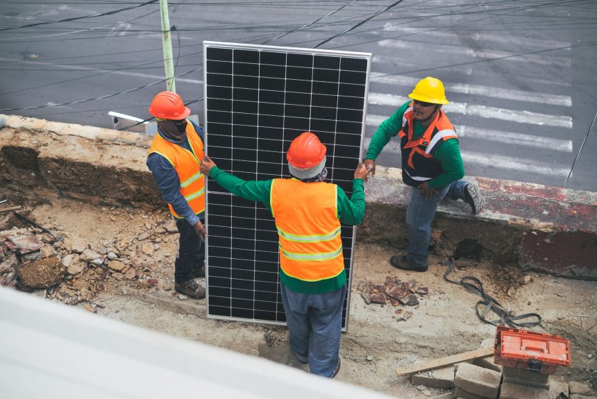 Trabalhadores usando equipamentos de proteção individual instalam painéis solares em um canteiro de obras.