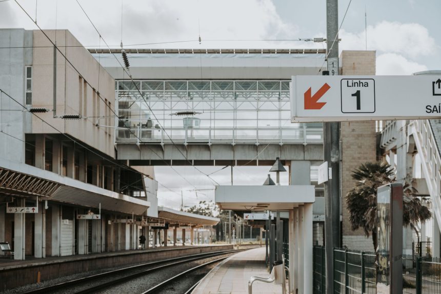 Plataforma de uma estação ferroviária urbana contemporânea em Lisboa, com linhas e estruturas de transporte.